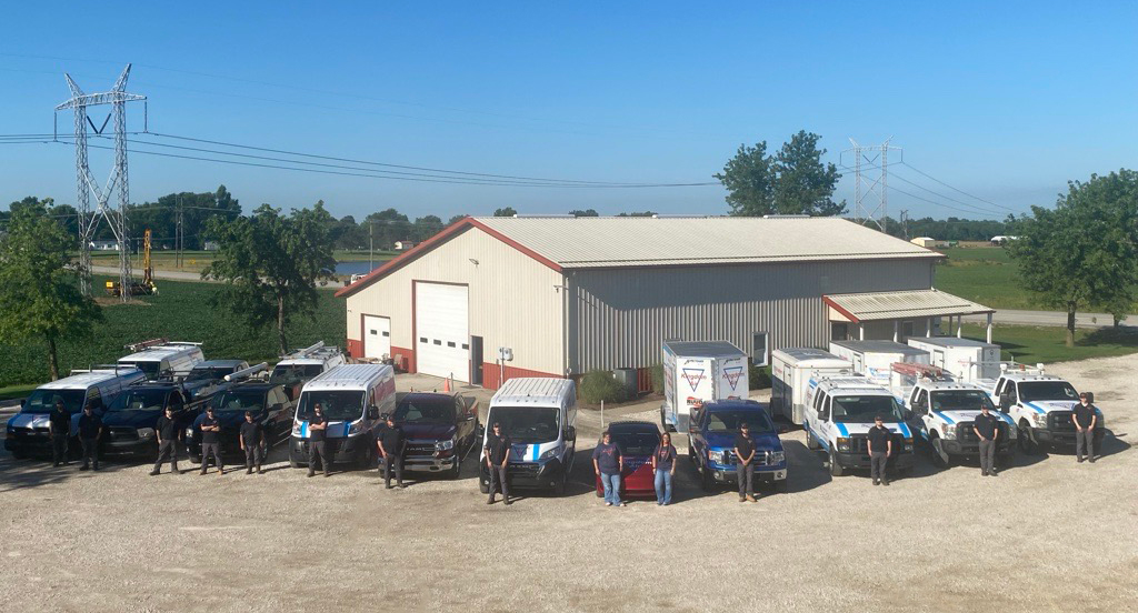 The Kingdom Air team of licensed HVAC technicians and plumbers, and office staff, standing with company service vans in front of the Kingdom Air headquarters.